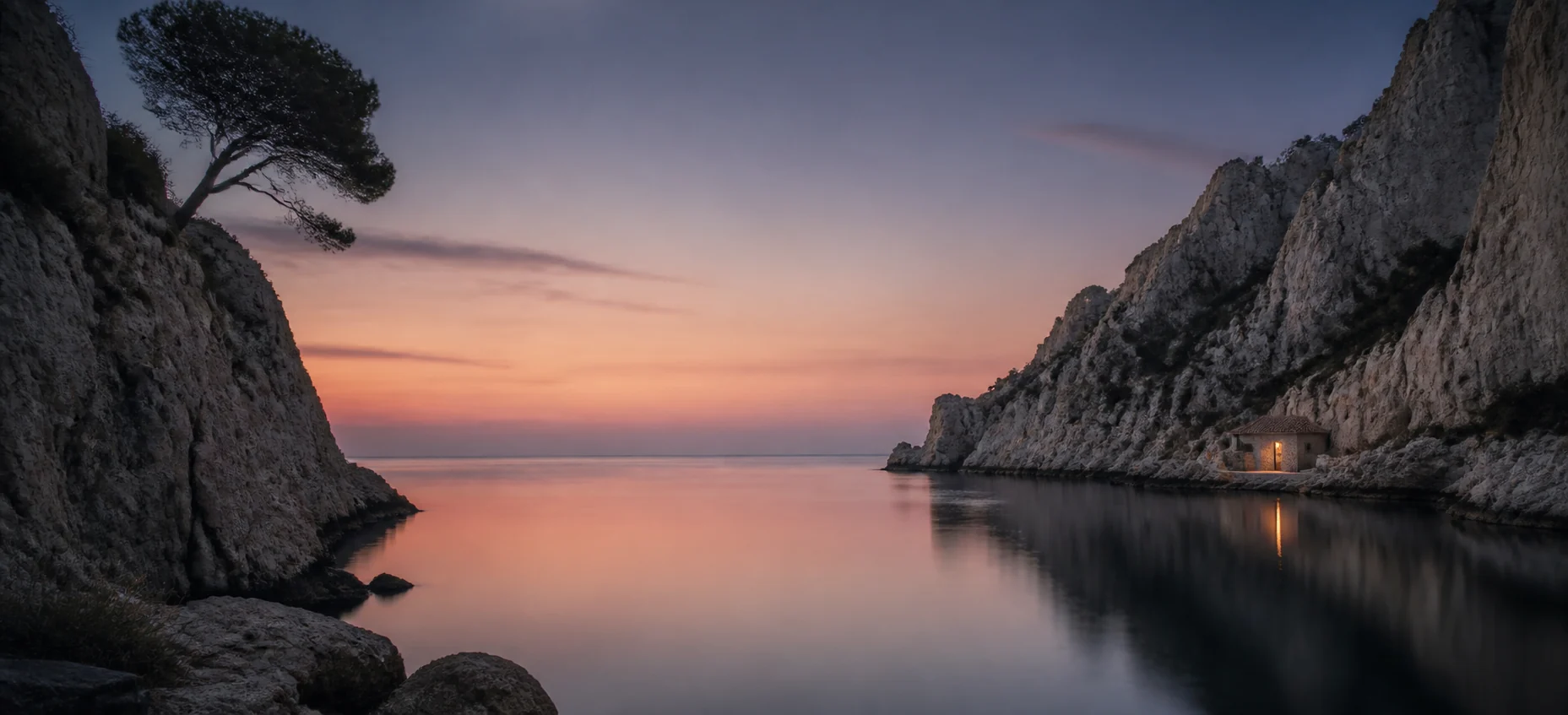 Une calanque paisible au crépuscule, un pin penché sur la mer et la lumière d’un cabanon